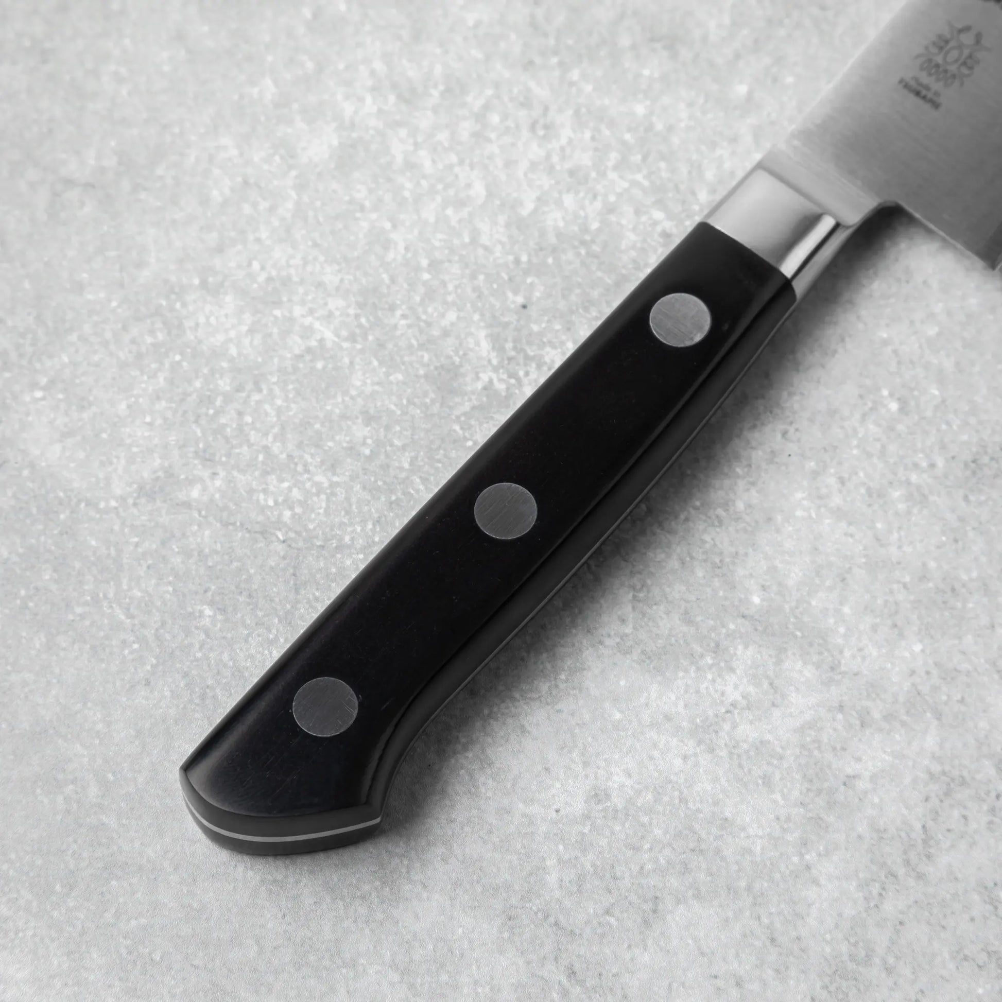 A close-up of the knife’s ergonomic black handle, secured with three rivets for durability and a comfortable grip.