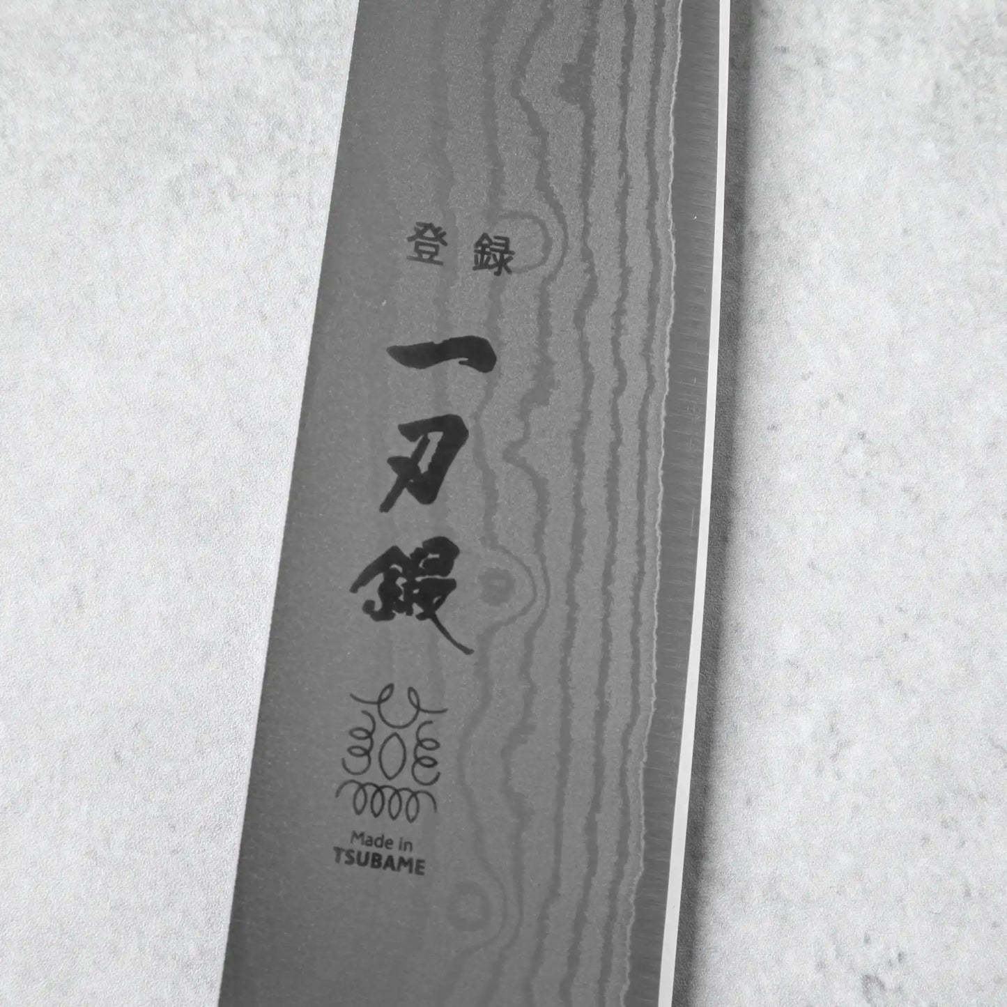 A close-up of the engraved logo and Japanese characters on the Damascus steel blade, emphasizing its craftsmanship and origin from Tsubame, Japan.