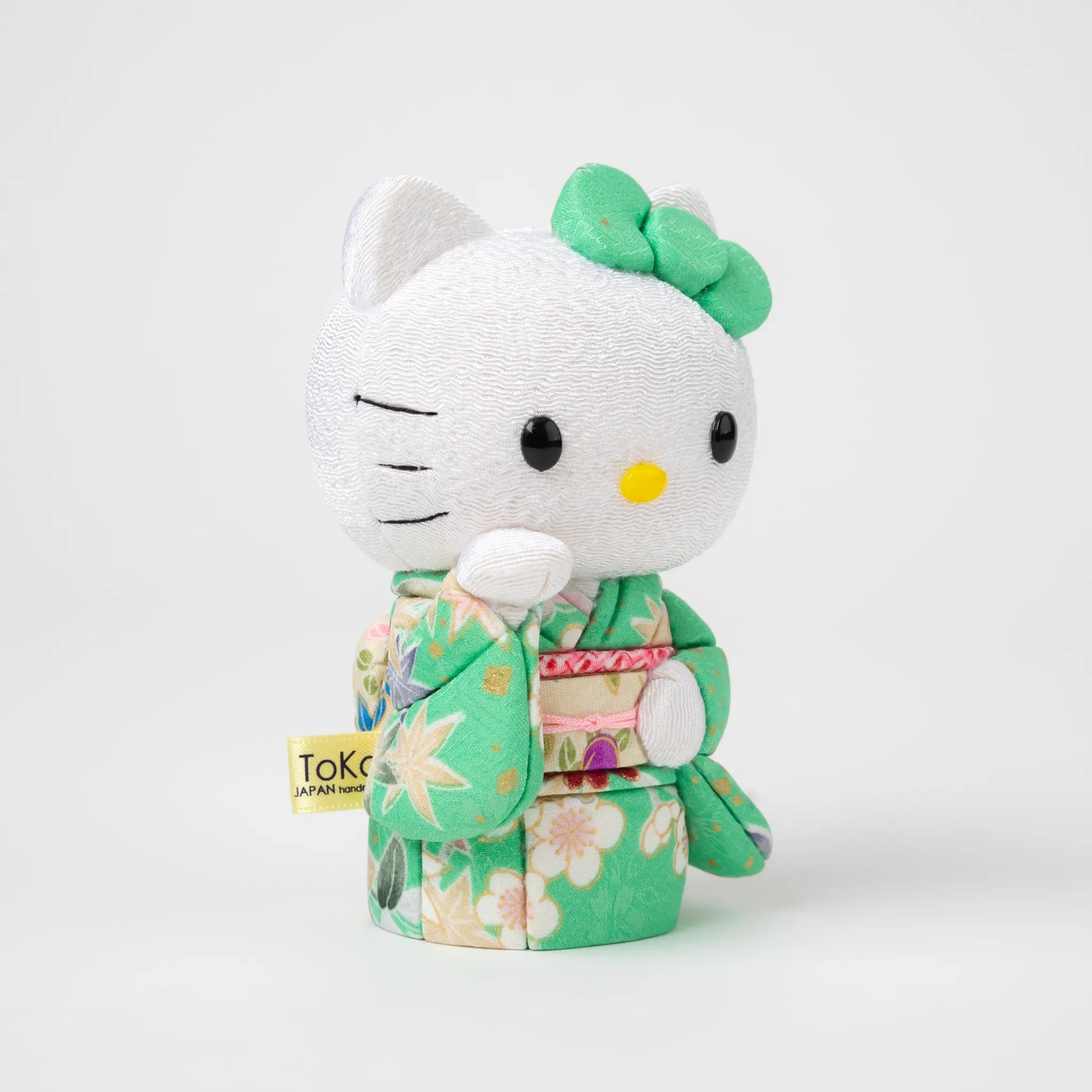 Angled view of the Edo Kimekomi Kimono Maneki Hello Kitty Green, highlighting the traditional fabric texture and floral design of the green kimono, with Hello Kitty’s arm raised in a welcoming gesture.