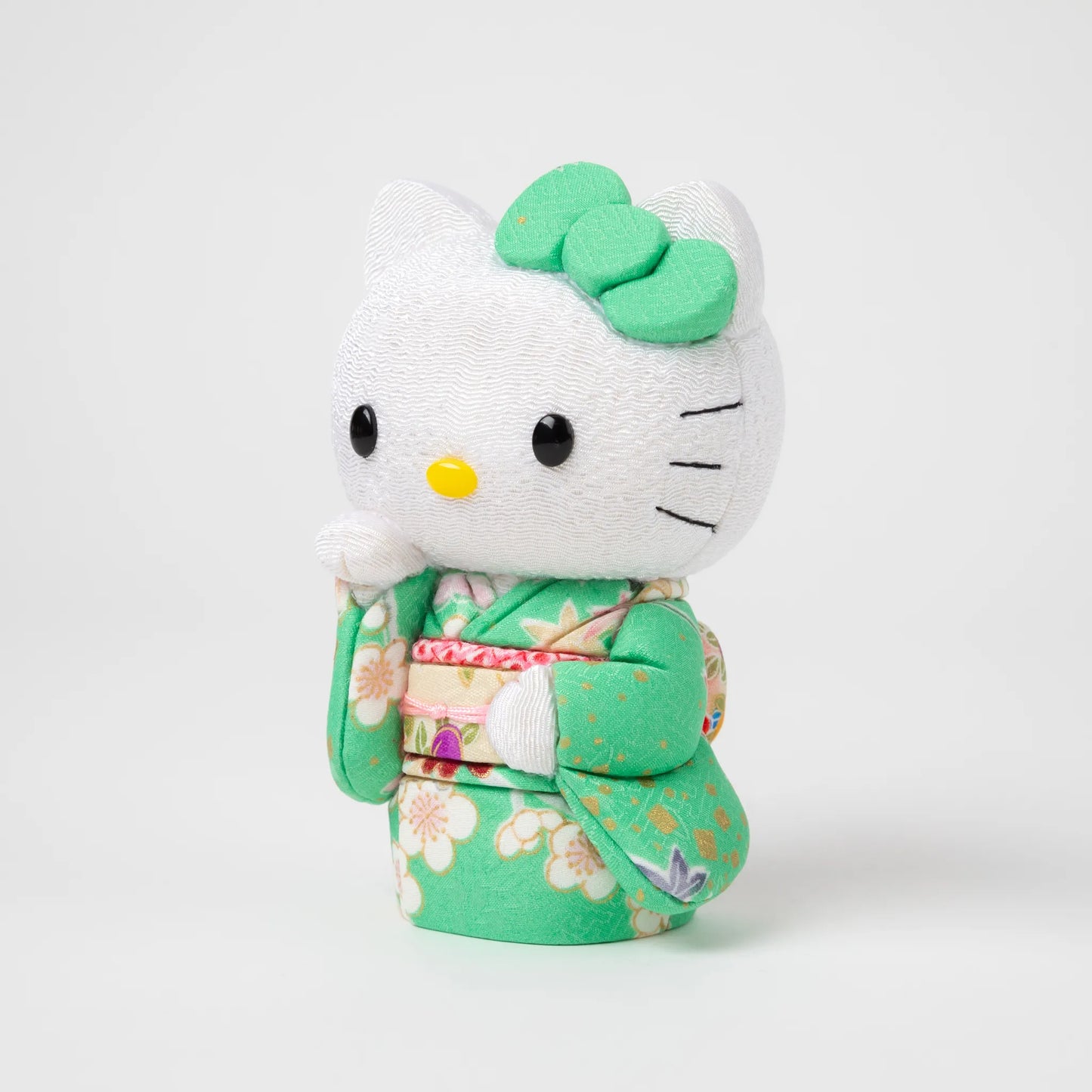 Side view of the Edo Kimekomi Kimono Maneki Hello Kitty Green, showcasing intricate details of the floral-patterned green kimono and a label indicating 'Toko Japan' attached to the kimono.