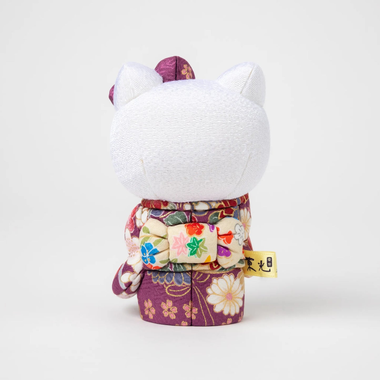 Back view of the Edo Kimekomi Kimono Maneki Hello Kitty Purple, revealing the detailed bow and floral patterns on the purple kimono, symbolizing the Edo Kimekomi doll craftsmanship.