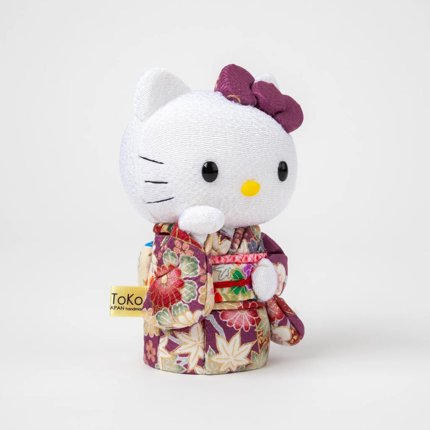 Angled view of the Edo Kimekomi Kimono Maneki Hello Kitty Purple, highlighting the traditional fabric texture and floral design of the purple kimono, with Hello Kitty’s arm raised in a welcoming gesture.