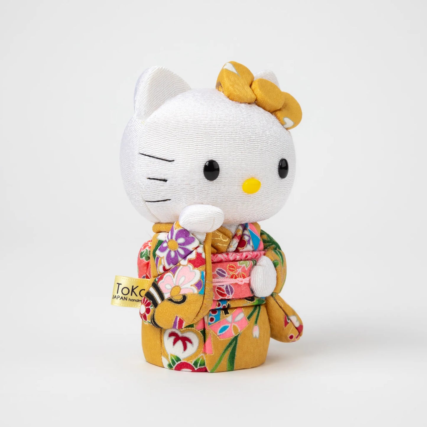 Angled view of the Edo Kimekomi Kimono Maneki Hello Kitty Yellow, highlighting the traditional fabric texture and floral design of the yellow kimono, with Hello Kitty’s arm raised in a welcoming gesture.