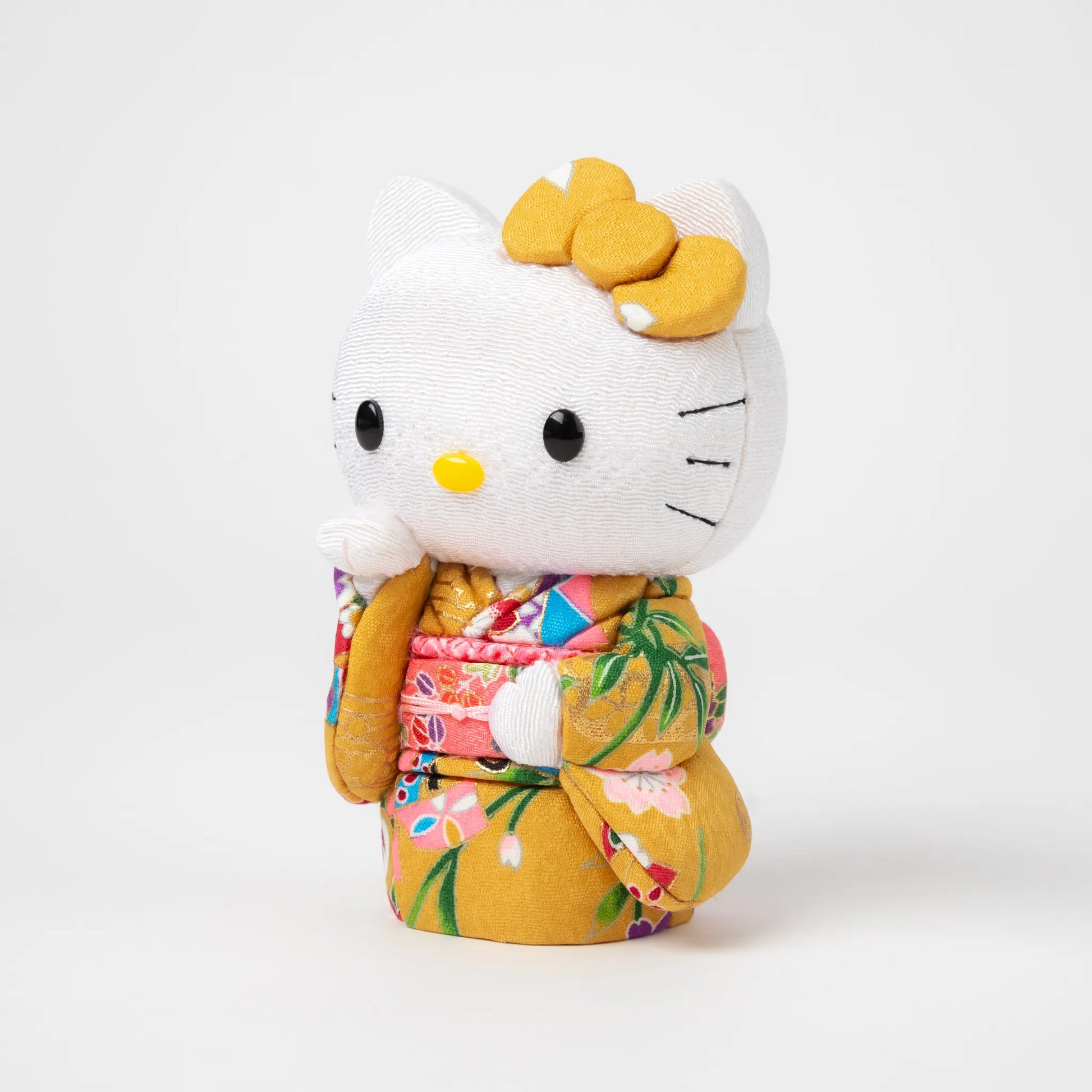 Side view of the Edo Kimekomi Kimono Maneki Hello Kitty Yellow, showcasing intricate details of the floral-patterned yellow kimono and a label indicating 'Toko Japan' attached to the kimono.