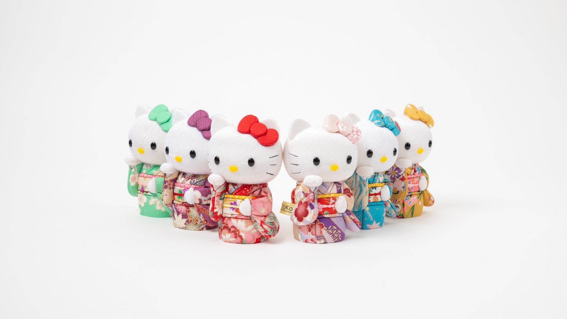 A line-up of Edo Kimekomi Kimono Maneki Hello Kitty figurines by Kakinuma Toko, showcasing an array of colors—red, blue, green, yellow, pink, and purple. The Hello Kitty figures are dressed in intricately designed kimonos with floral motifs, representing a blend of Japanese tradition and modern kawaii culture.