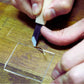 Close-up of a person using a wood carving chisel to carve a square pattern into a wooden surface with precision.