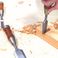 A detailed shot of a woodworker using the Kakuri Damascus chisel set, carving a notch into a wooden block with other chisels laid nearby.