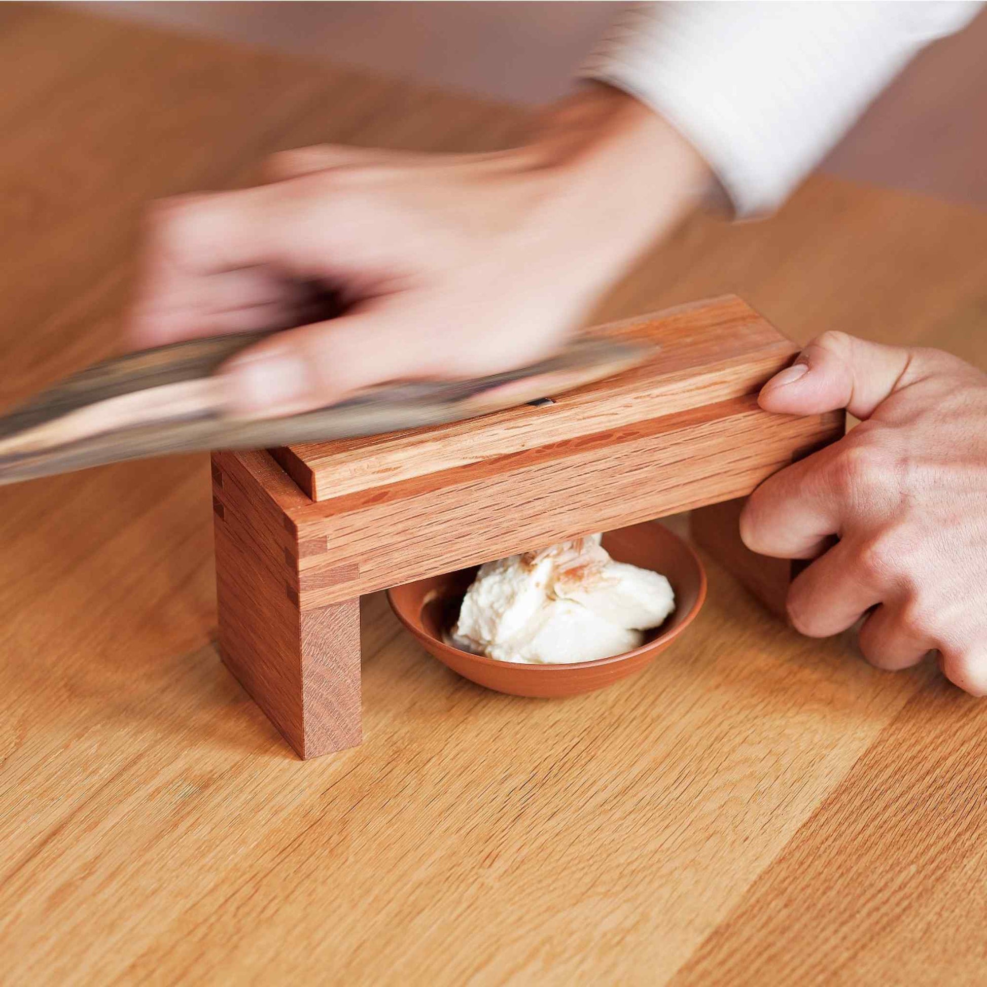  A demonstration image showing hands operating the shaver, with bonito flakes being shaved onto a small plate underneath.