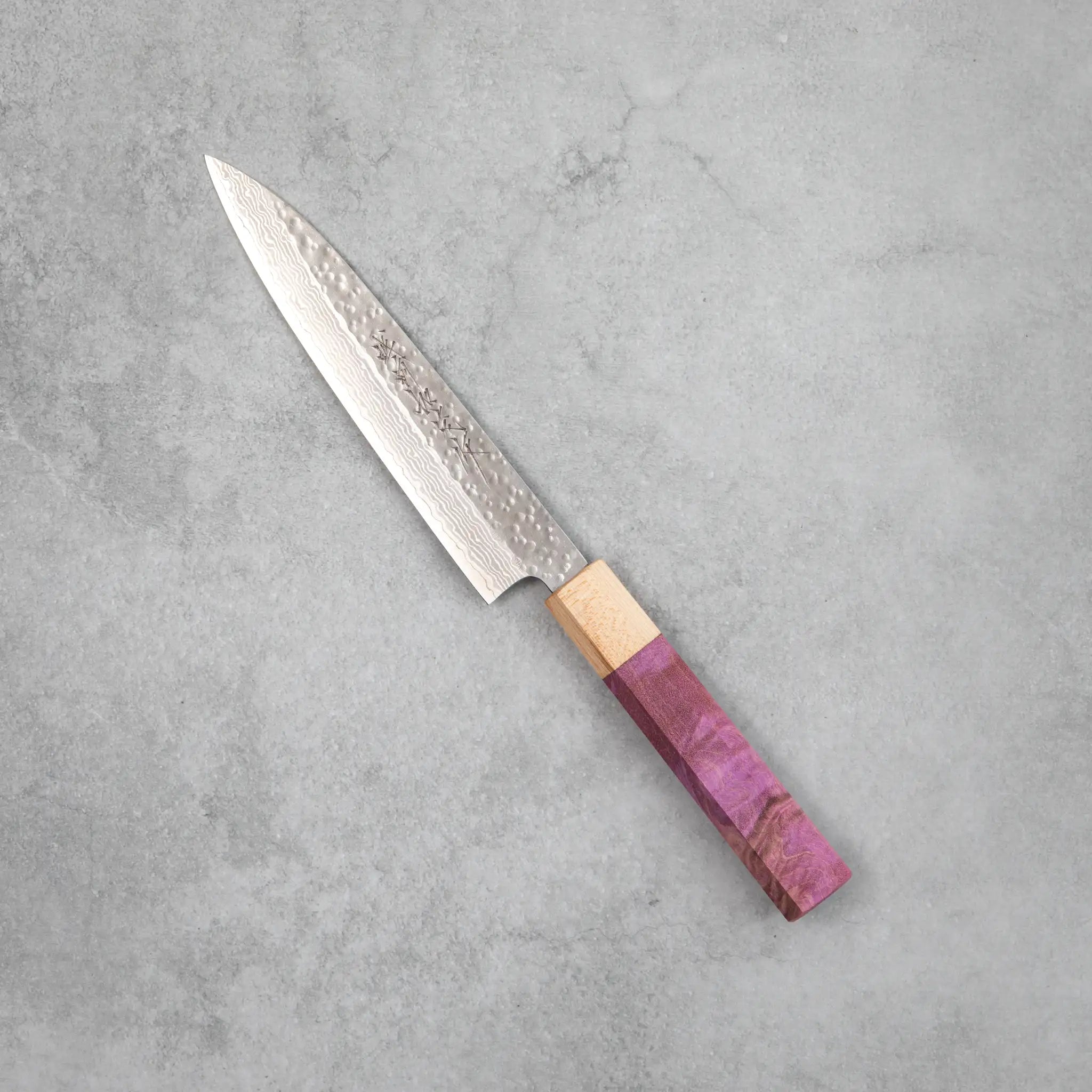 Side view of the Kamo Hamono Shizuku petty knife with purple stabilized maple handle, pale maple bolster, and a narrow pointed VG10 Damascus blade with rounded tsuchime hammer marks across the upper surface.