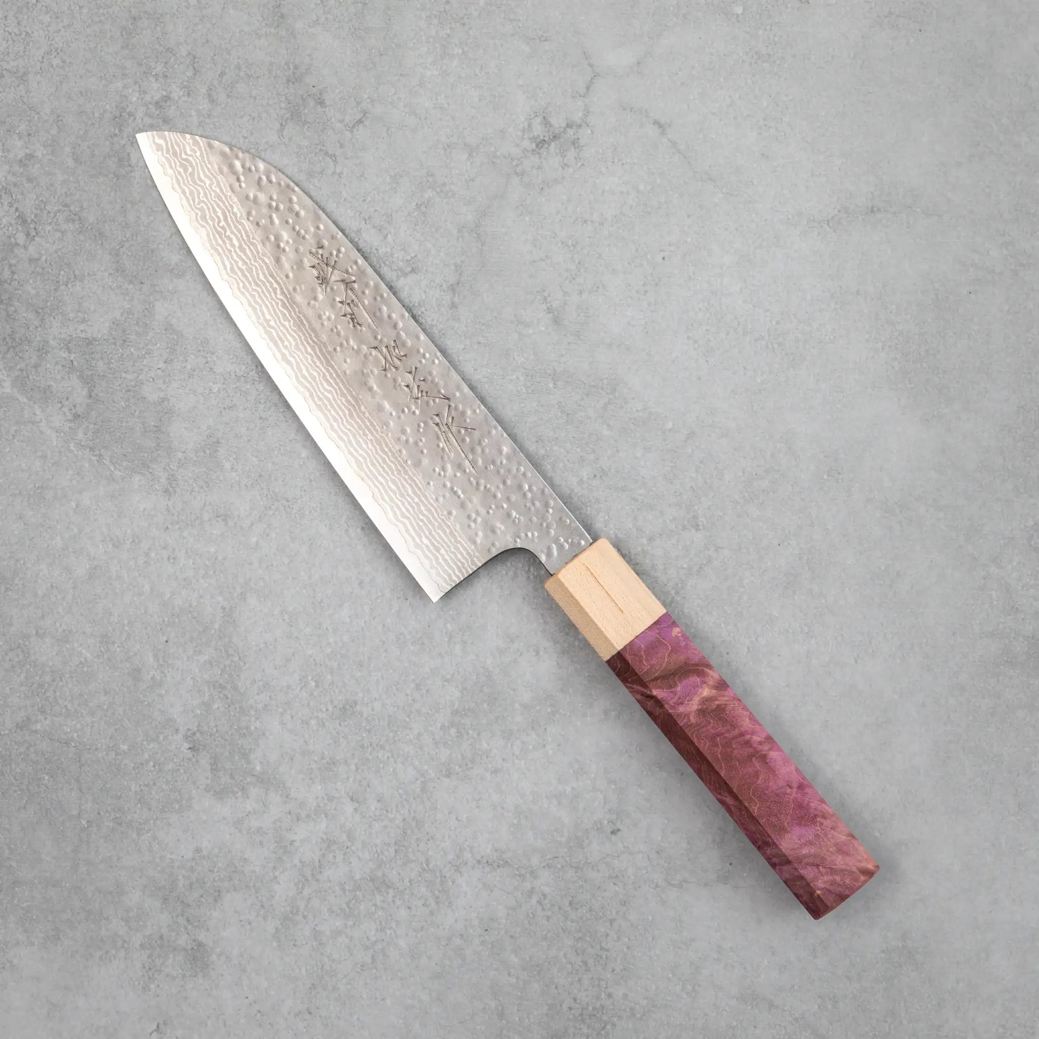 Side view of the Kamo Hamono Shizuku santoku knife with purple stabilized maple handle, pale maple bolster, and a VG10 Damascus blade with rounded tsuchime hammer marks across the upper surface.