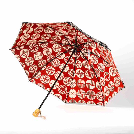 Isa Moyō Folding Umbrella opened, revealing the Pine Tree motif on a red background, with the bamboo handle visible.