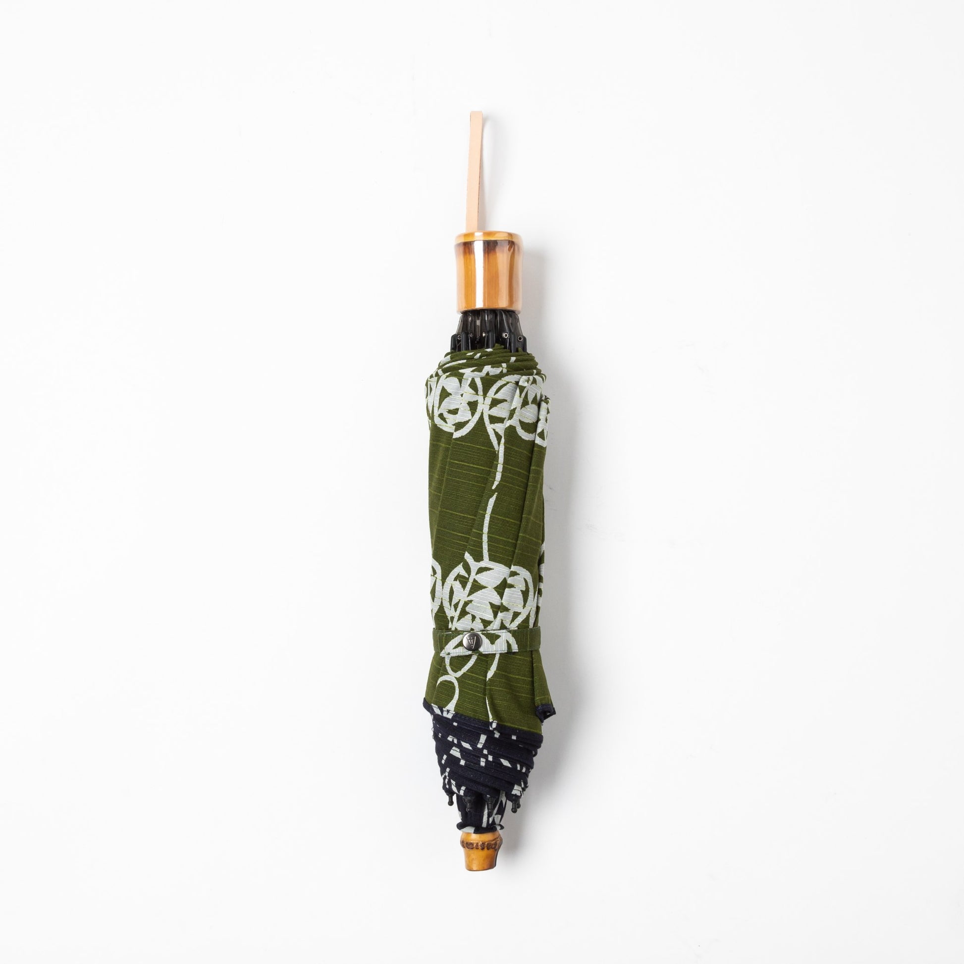 A folded Isa Moyō Folding Umbrella displaying the Rosary Vine motif in deep navy with an inner lining of contrasting green.