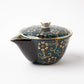 Kutani Aochibu Tessen teapot with a dark blue base, adorned with intricate gold floral patterns and a dotted turquoise background, featuring a small spout and a fitted lid.