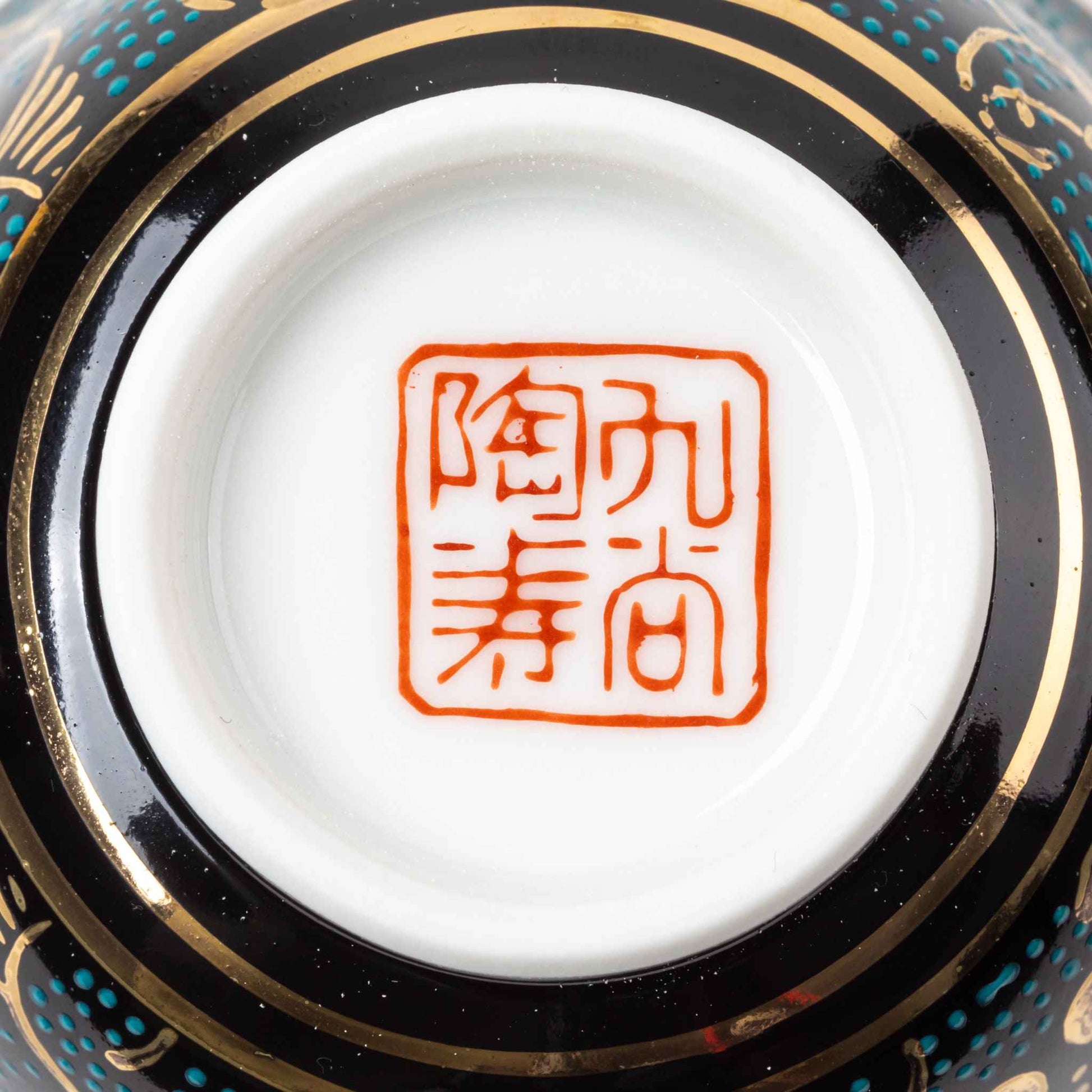 Close-up of the bottom of a Kutani Aochibu Tessen tea cup, showing the traditional Kutani red seal marking on the white porcelain base.