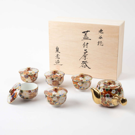 Kutani Blooming Flowers tea set featuring a teapot and five tea cups with lids, all decorated in colorful chrysanthemum patterns with gold detailing, placed alongside a wooden storage box with Japanese calligraphy.