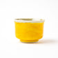 A view of the sake cup's plain side, showing the solid yellow glaze without any painted details.