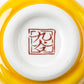 A close-up of the base of the sake bottle showing the red Kutani maker's mark against the yellow background.