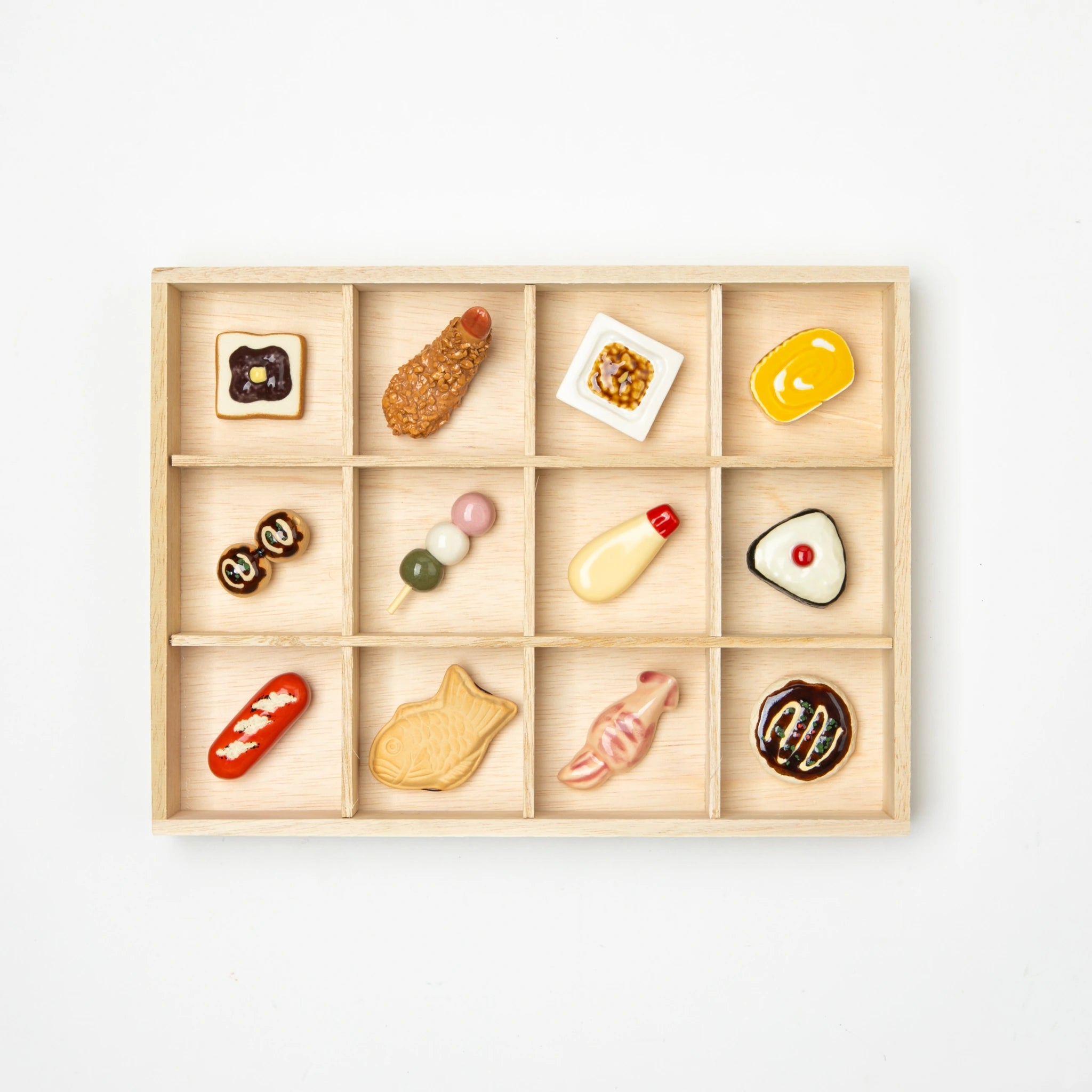 Set of 12 ceramic chopstick rests shaped like Japanese foods, neatly arranged in a wooden box with compartments.