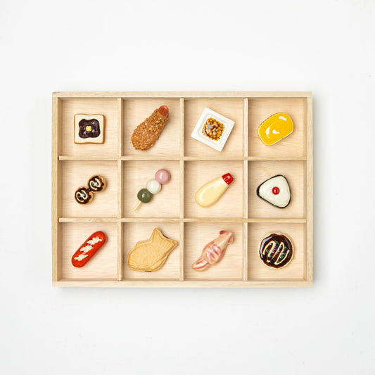 Set of 12 ceramic chopstick rests shaped like Japanese foods, neatly arranged in a wooden box with compartments.