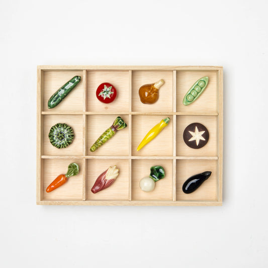 Set of 12 ceramic chopstick rests shaped like assorted vegetables, organized in a wooden display box.