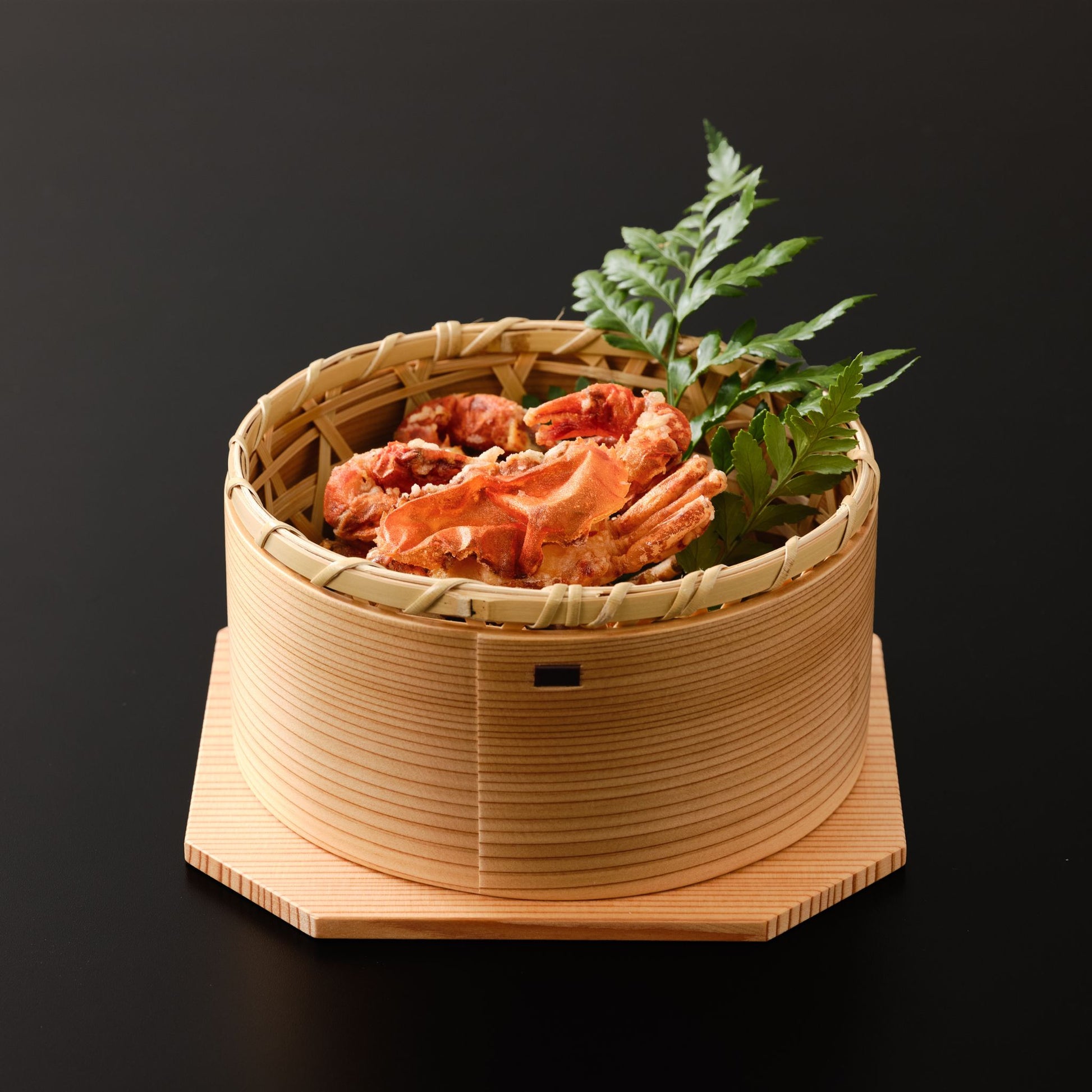 A bamboo basket filled with fried crab, placed inside a wooden bowl with an octagonal base.