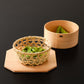 A bamboo basket with green beans inside, set alongside an empty wooden bowl and octagonal base on a dark surface.