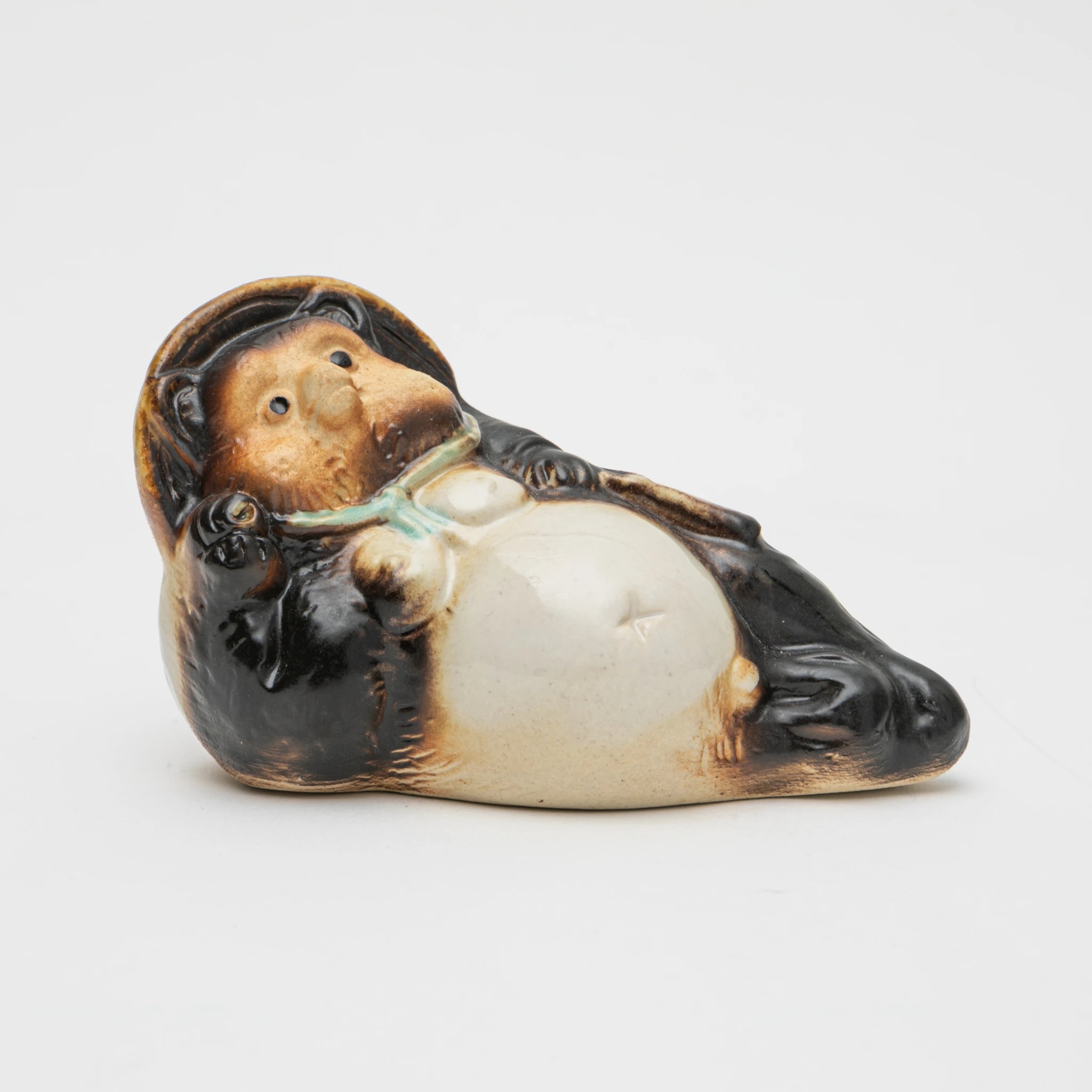 Three-quarter view of the Maruichi Shigaraki ware Reclining tanuki figurine, showing the figure lying on its back with belly upward, hat tilted, and a sake flask held loosely in one paw.