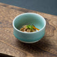 A Nabeshima celadon porcelain tea cup filled with a savory dish, showcasing the cup's use for food presentation.