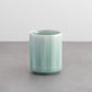 Nabeshima Celadon Porcelain Teacup showcasing its vertical grooves and subtle green color, placed on a gray surface.