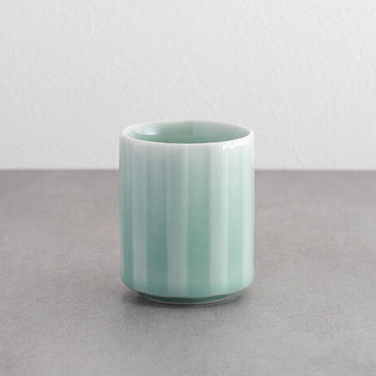 Nabeshima Celadon Porcelain Teacup showcasing its vertical grooves and subtle green color, placed on a gray surface.