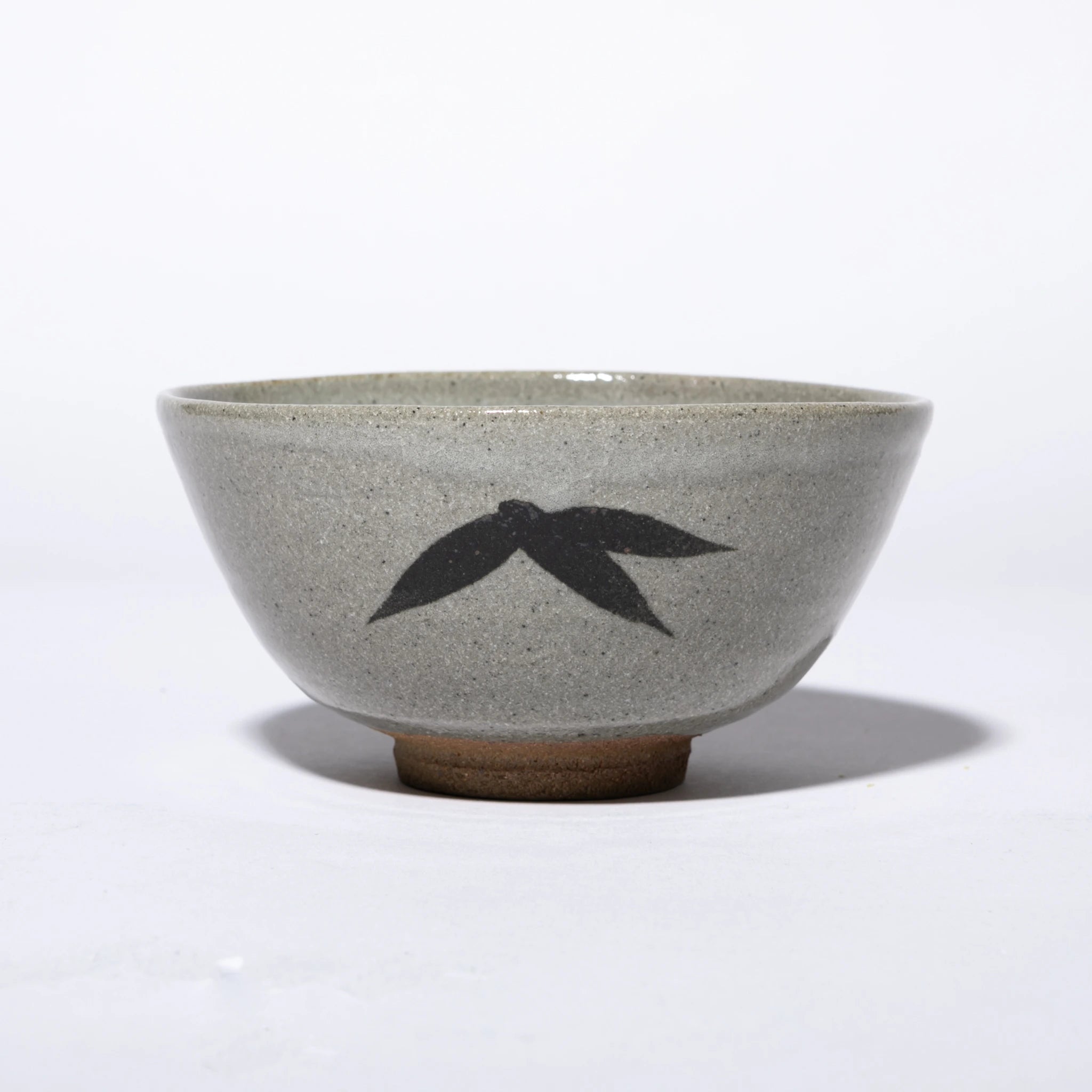 Front view of the Nakazato Tarouemon E-Karatsu matcha bowl with bamboo motif, showing a wide deep form with pale grey feldspathic glaze, a dense iron-oxide bamboo leaf cluster on the exterior wall, and an unglazed sandy clay foot ring.