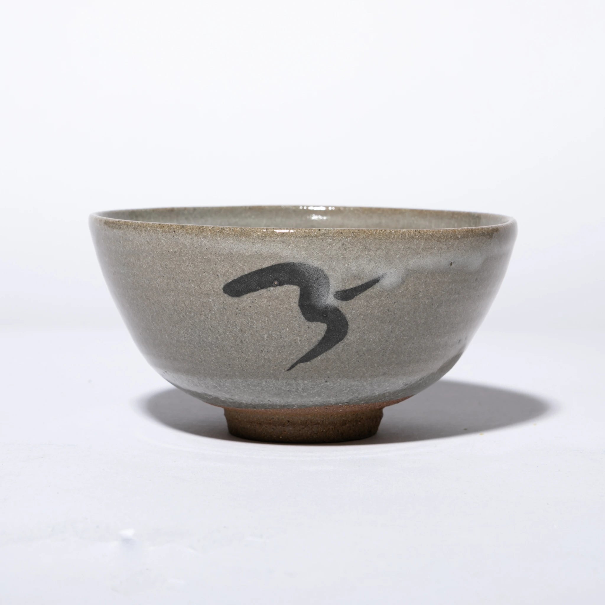 Front view of the Nakazato Tarouemon E-Karatsu matcha bowl with bird motif, showing a wide deep form with pale grey feldspathic glaze, an iron-oxide bird in flight painted on the exterior wall, and an unglazed sandy clay foot ring.