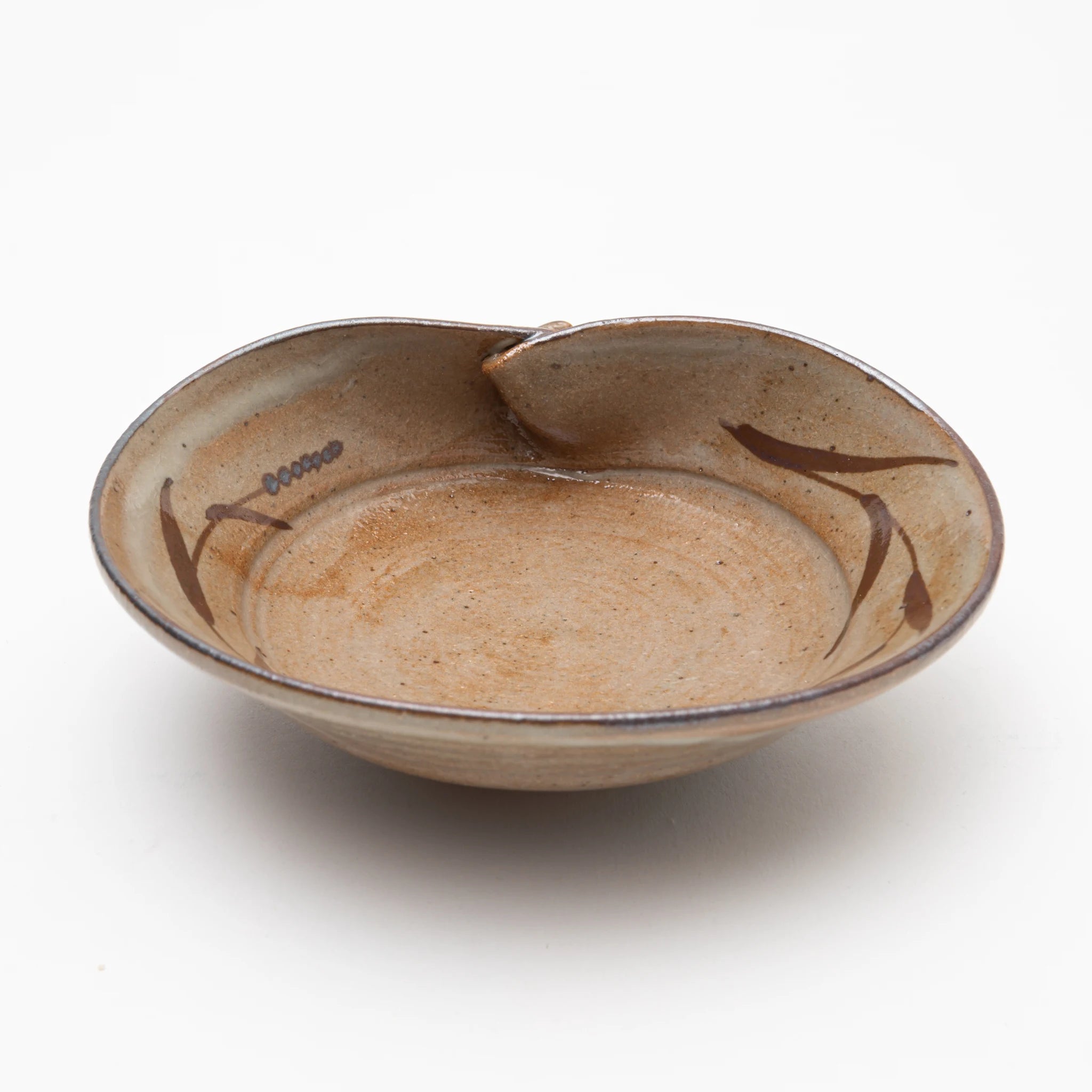 Three-quarter view of the Nakazato Tarouemon E-Karatsu clam shape mukozuke serving dish, showing a wide shallow form with a pinched rim, warm sandy stoneware ground, and sparse iron-oxide brushwork of leaf strokes and dotted marks across the interior.