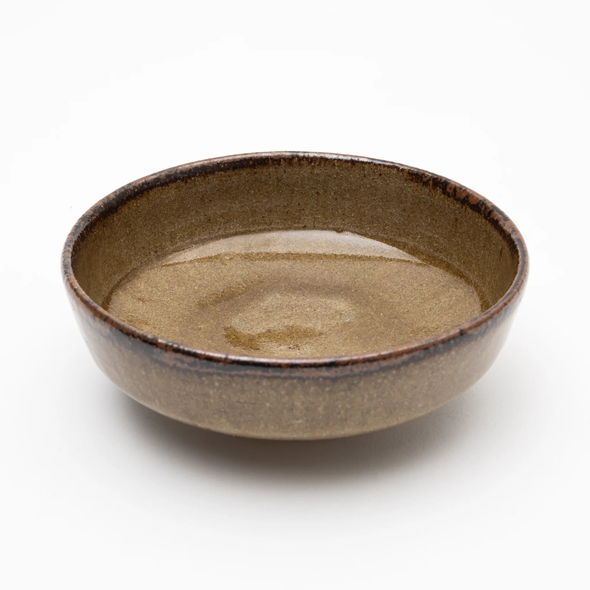 Three-quarter view of the Nakazato Tarouemon Yellow Karatsu mukozuke serving dish, showing a round open form with warm ochre ash glaze across the interior deepening to near-black at the thickened rim.