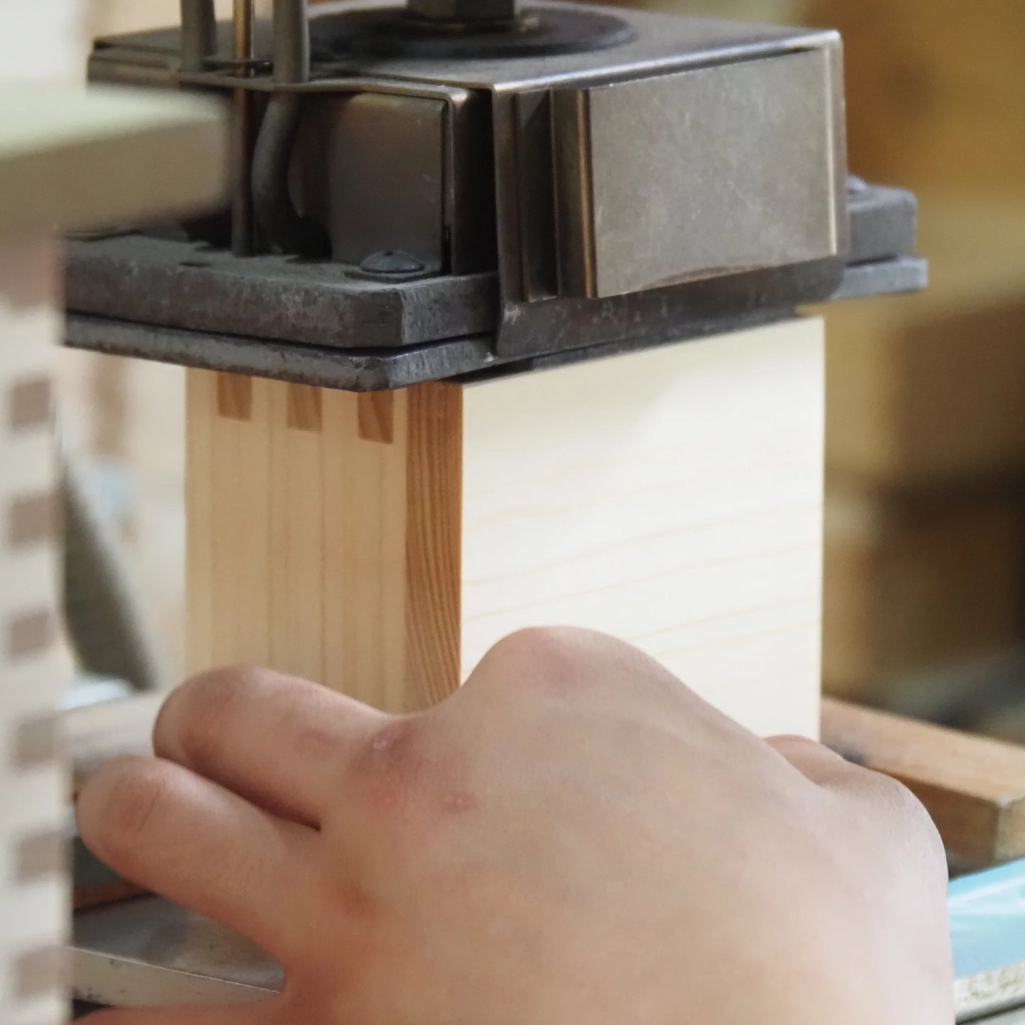 Close-up of a craftsman's hand pressing a wooden masu cup under a metal stamping machine.