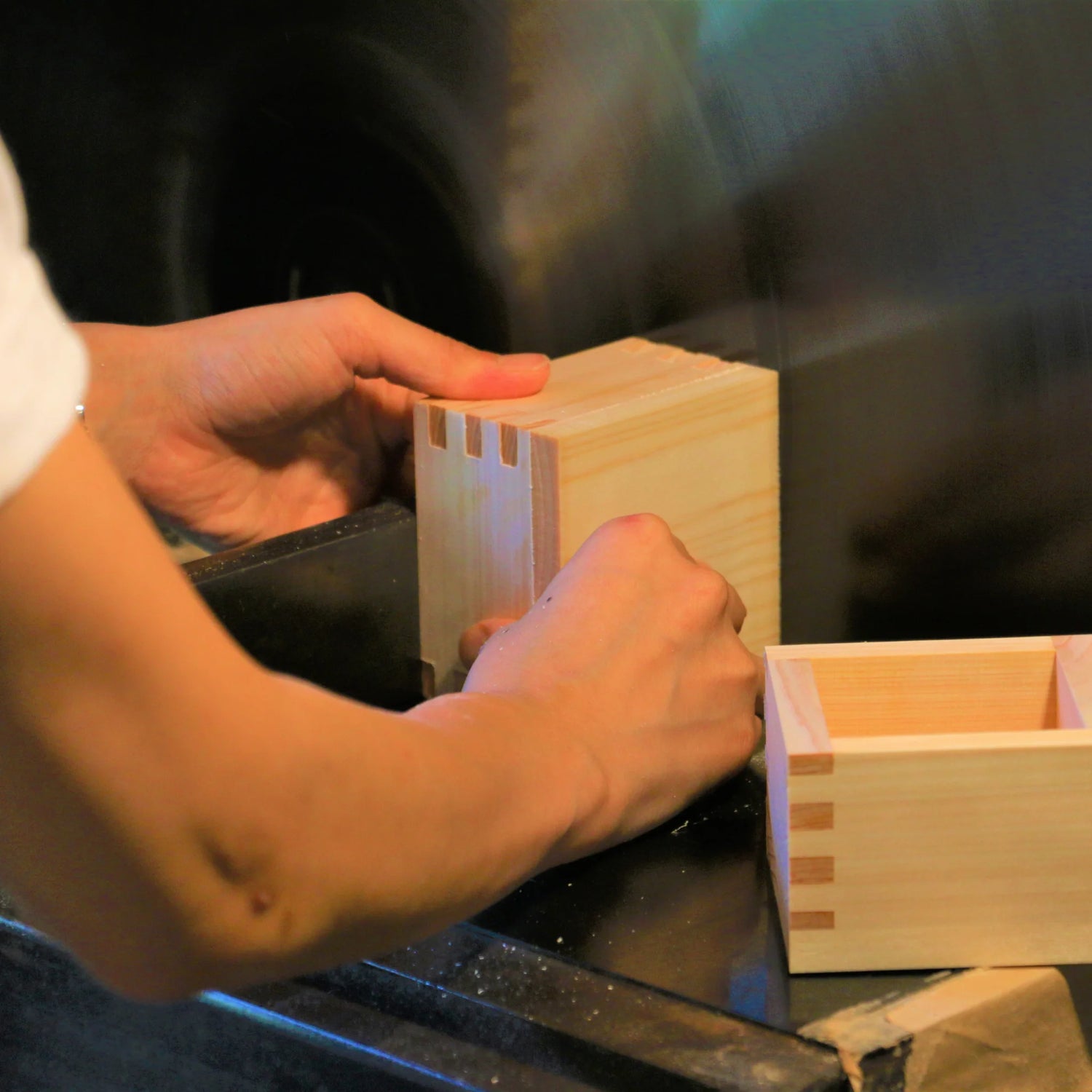 A craftsman assembling wooden masu cups by aligning dovetail joints on a workstation.