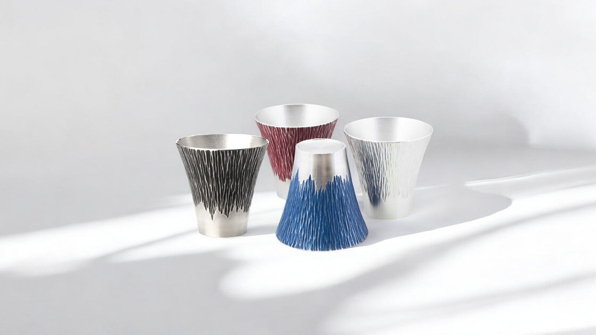 A set of four Osaka Suzuki Mt. Fuji Tumblers in various colors, including black, red, blue, and silver. Each tumbler features a textured design that mimics the ridges of Japan’s iconic Mt. Fuji, showcasing a blend of traditional and modern Japanese metalwork craftsmanship.