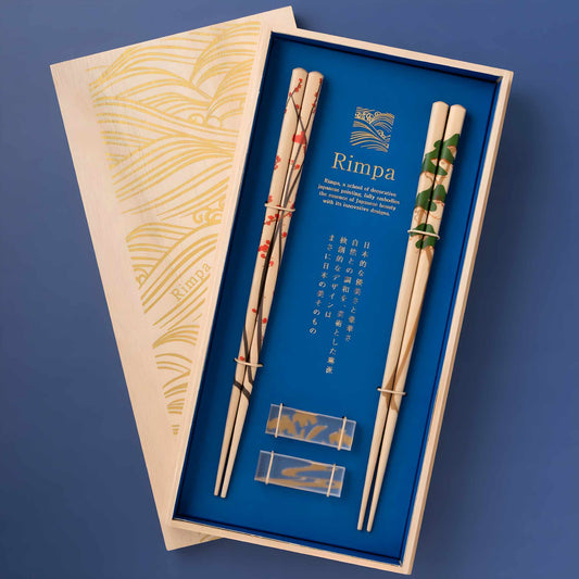 Set of Rimpa-style natural wood chopsticks with two pairs featuring plum blossom and pine tree designs, presented in an elegant wooden box with gold wave motifs, complete with transparent chopstick rests.