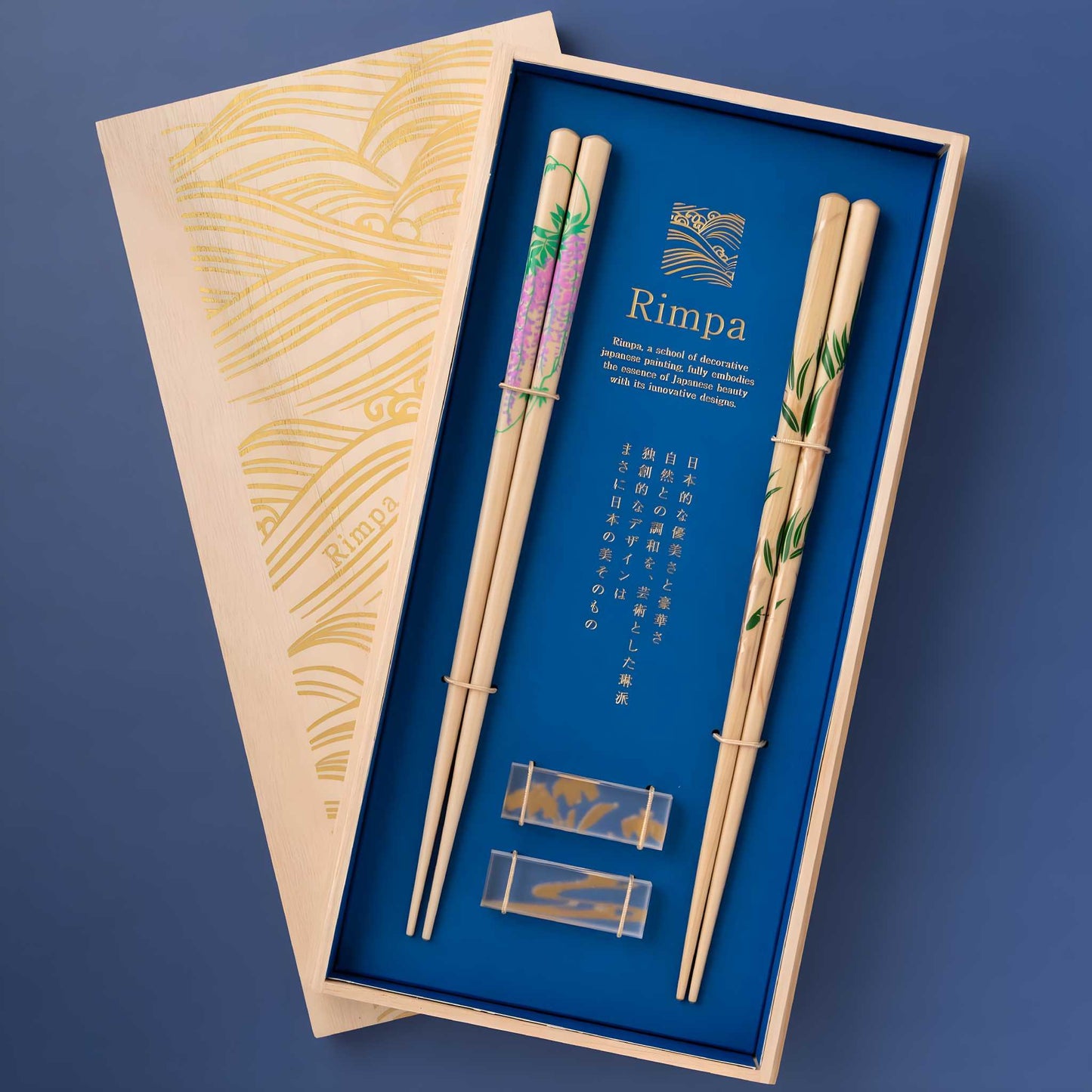 Elegant set of Rimpa-style chopsticks displayed in a decorative wooden box with intricate gold wave patterns. The set includes two pairs of chopsticks featuring delicate Wisteria and Bamboo designs, accompanied by chopstick rests.