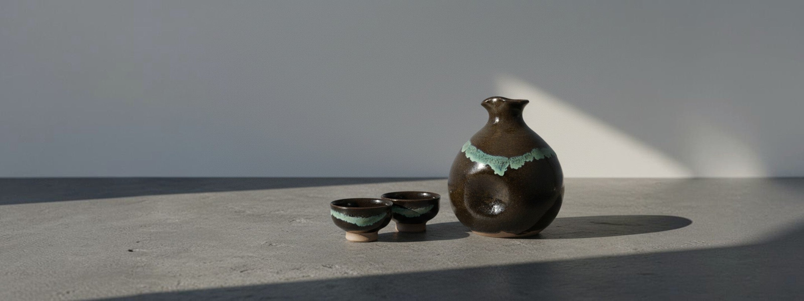 Two ceramic sake cup and a sake carafe on a concrete surface with a gray background