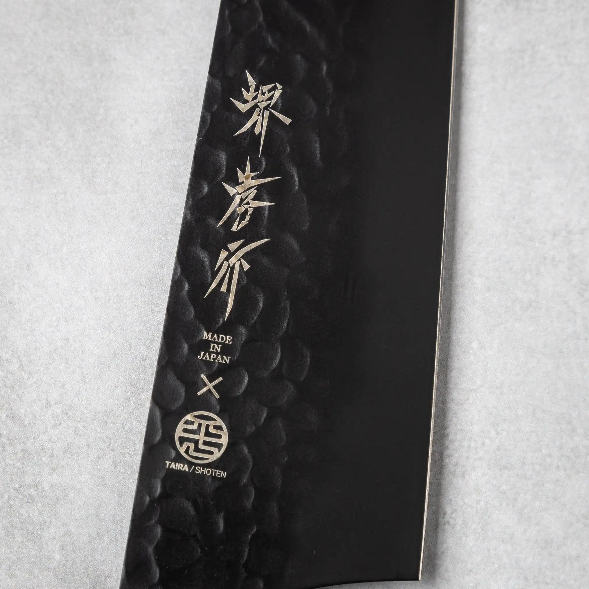 Close-up of the blade engraving on the Sakai Takayuki Kurokage VG10 petty knife, featuring Japanese characters and the "Made in Japan" emblem on the hammered black surface.