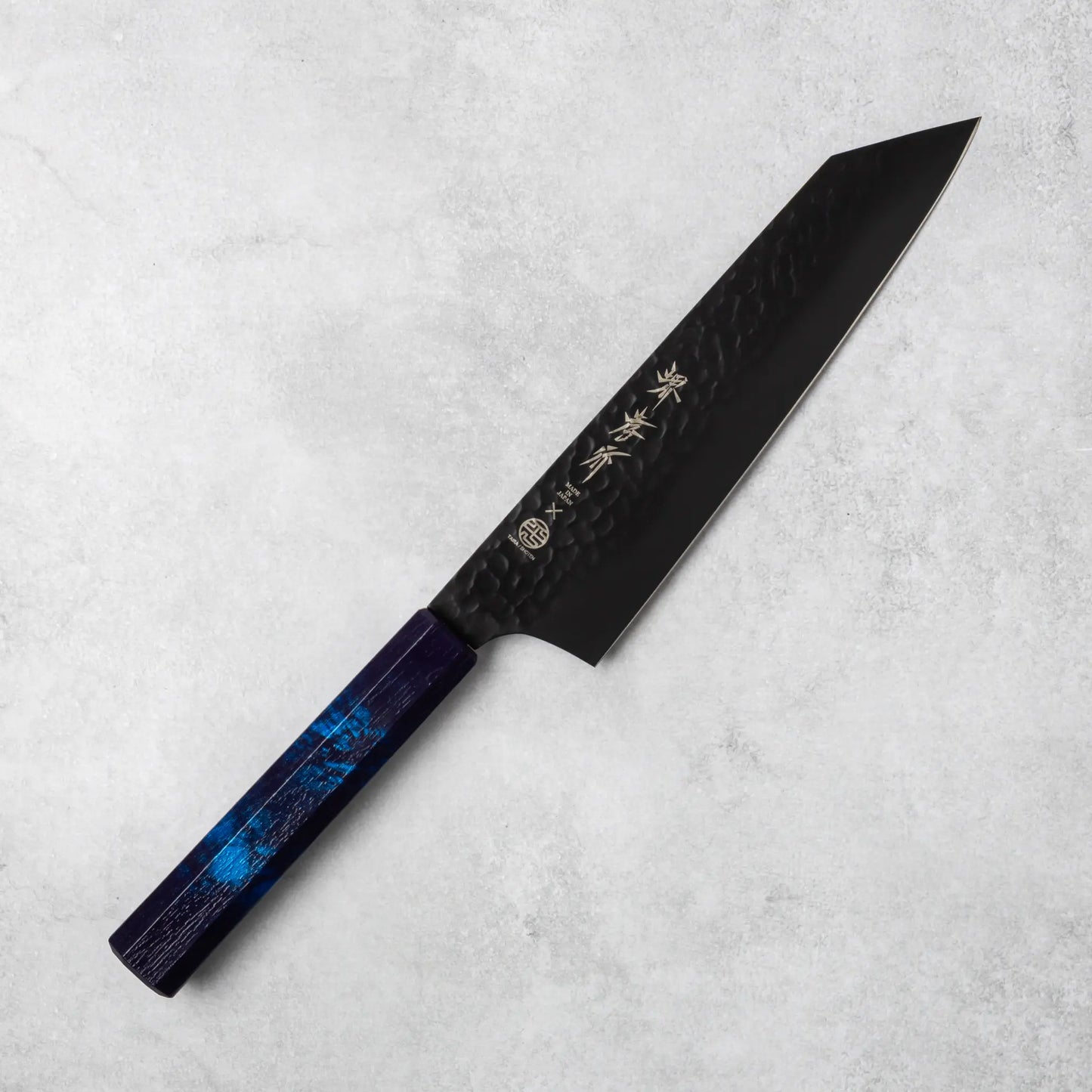 Sakai Takayuki Kurokage VG10 petty knife, featuring a hammered black blade and rich burgundy resin handle, positioned diagonally on a light stone surface.