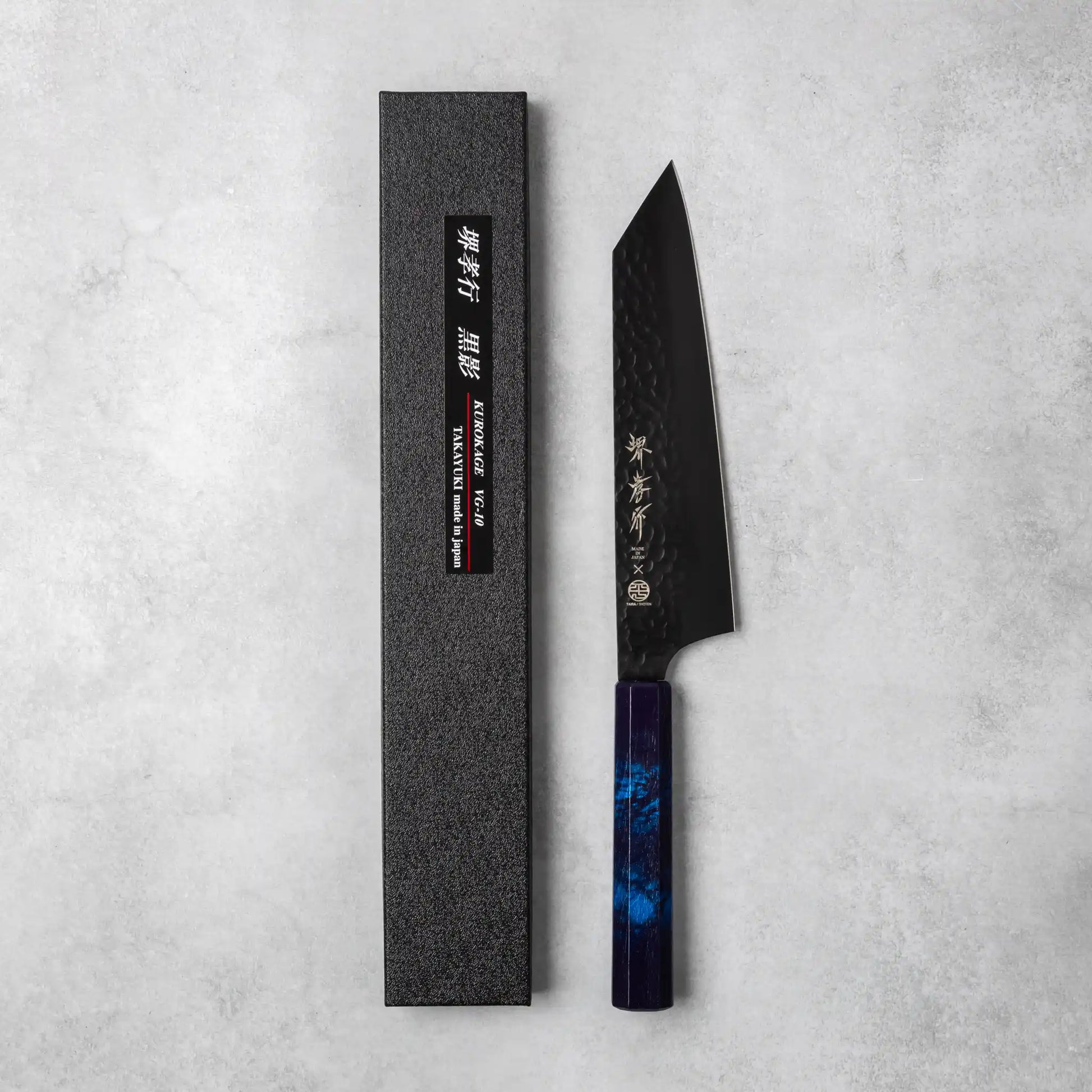 A Sakai Takayuki Kurokage VG10 petty knife with a hammered black blade and a luxurious burgundy resin octagonal handle, displayed alongside its black textured packaging on a neutral background.