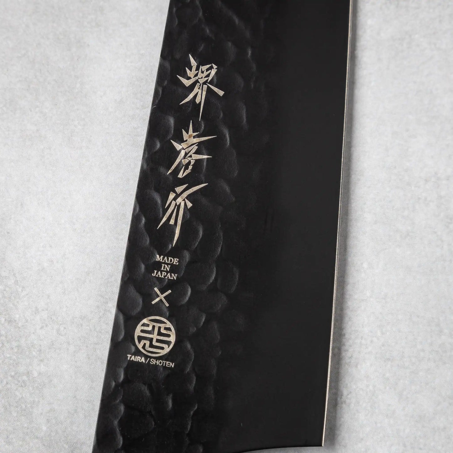 Close-up of the engraved blade on the Sakai Takayuki Kurokage VG10 Kengata chef knife, featuring Japanese characters and a "Made in Japan" emblem on its hammered black surface.