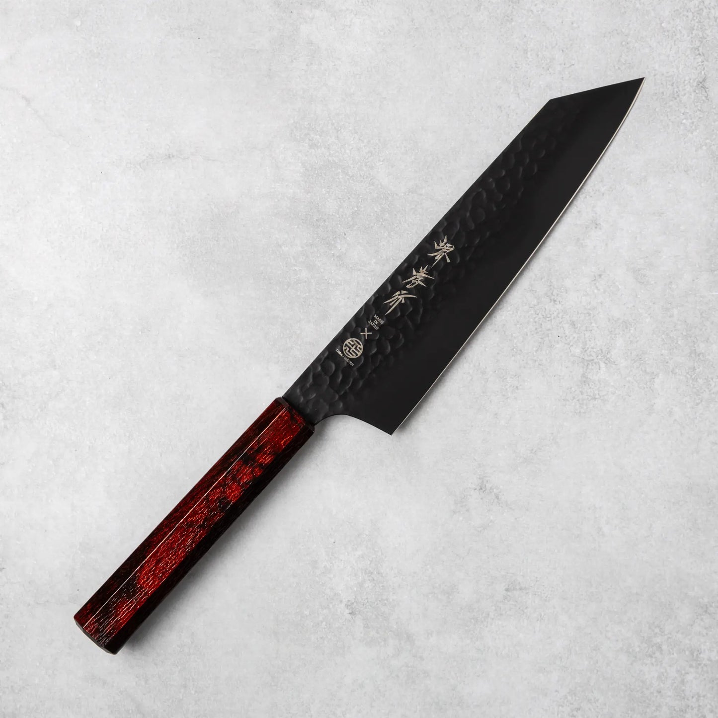 Sakai Takayuki Kurokage VG10 Kengata chef knife, featuring a long hammered black blade with a sharp pointed tip and a luxurious burgundy resin handle, positioned diagonally on a light stone surface.