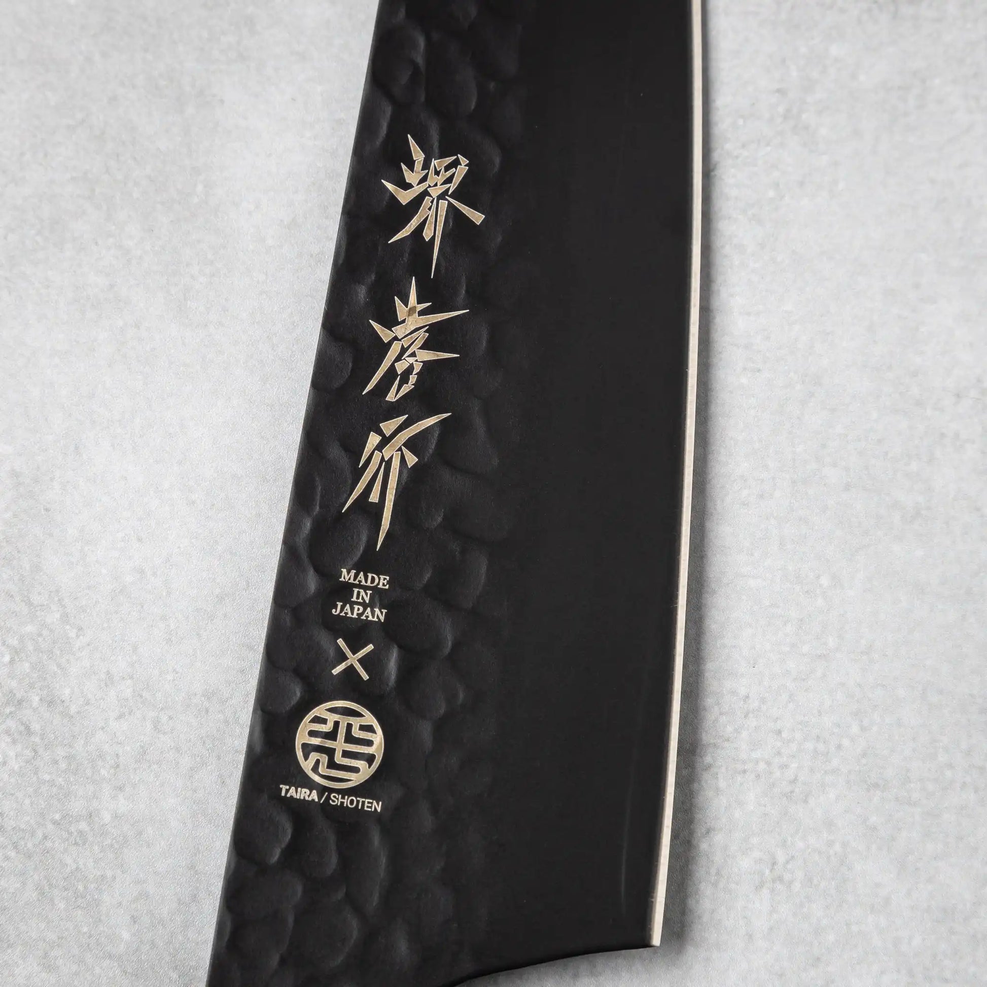 Engraved logo and branding details on the hammered black blade of the Sakai Takayuki Kurokage VG10 Kengata Santoku Knife.