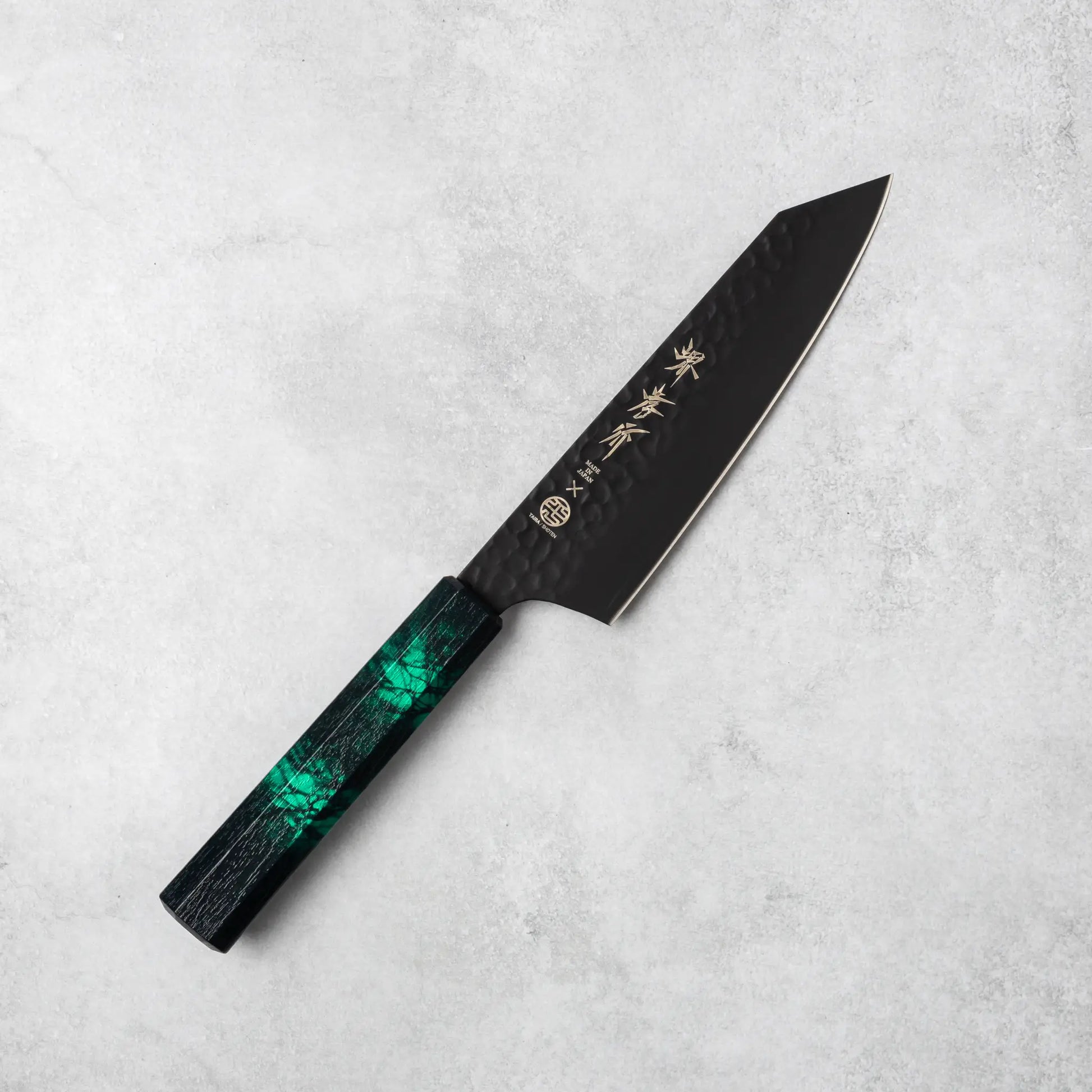 Full view of the Sakai Takayuki Kurokage VG10 Kengata Santoku Knife featuring a hammered black blade and green handle on a gray surface.