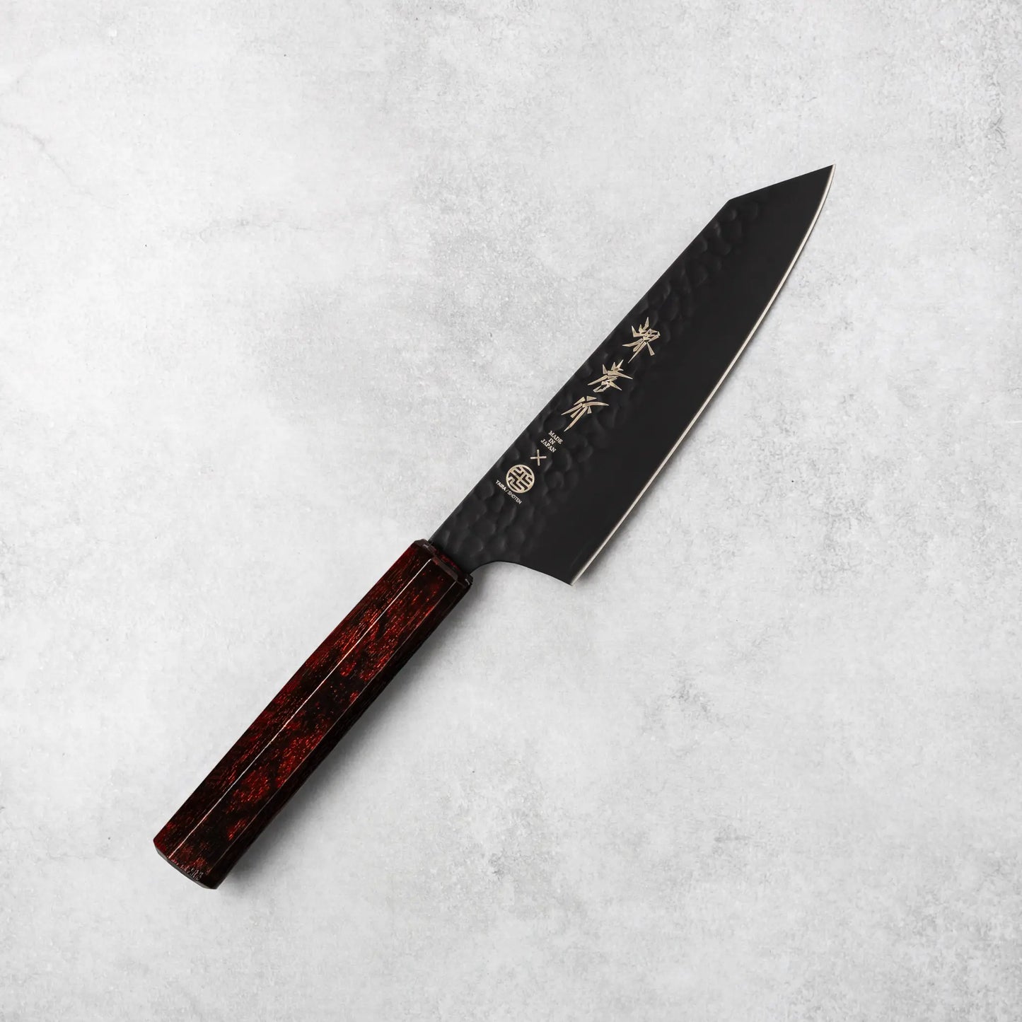 Full view of the Sakai Takayuki Kurokage VG10 Kengata Santoku Knife showcasing its hammered black blade and burgundy handle on a textured gray surface.