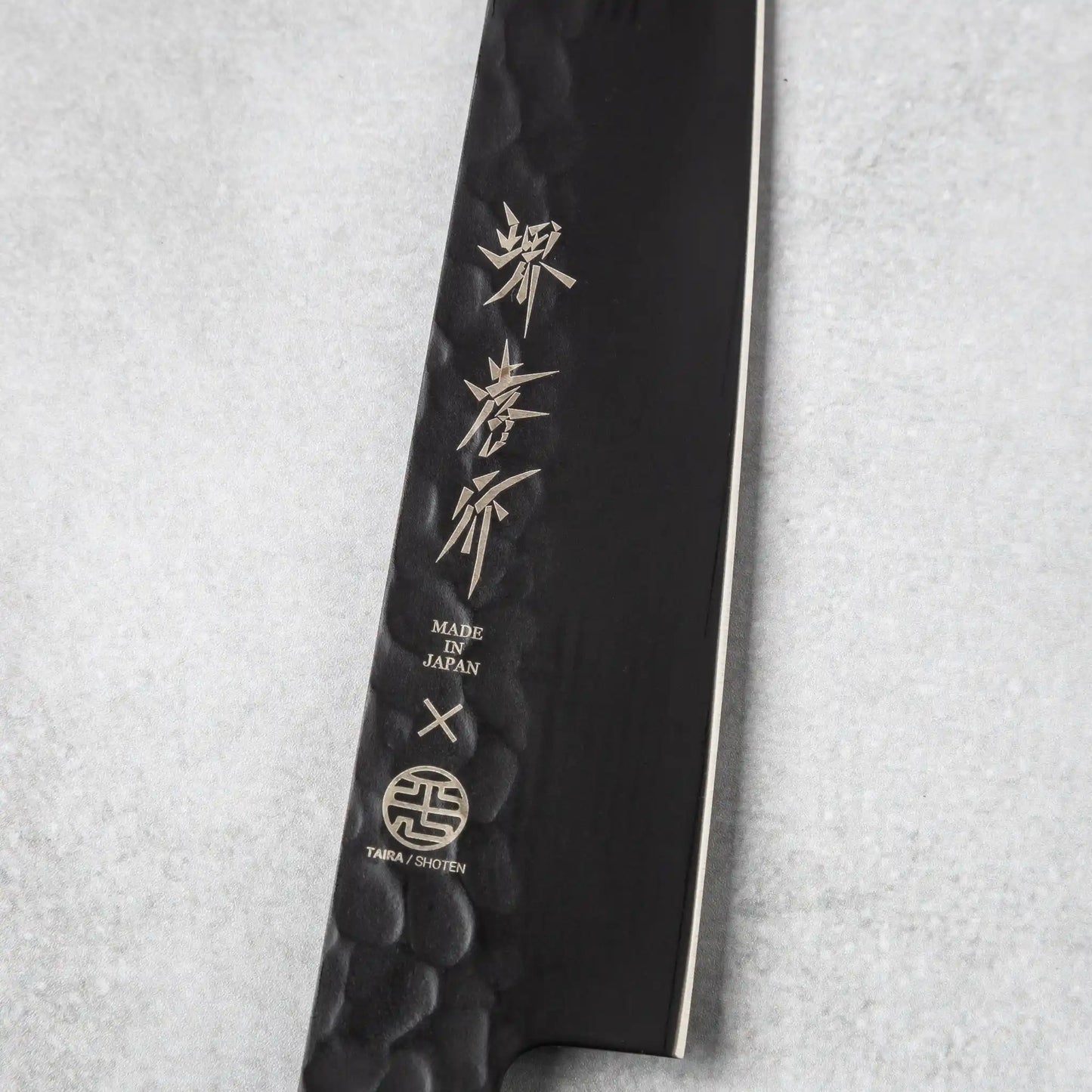 Close-up of the blade engraving on the Sakai Takayuki Kurokage VG10 petty knife, featuring Japanese characters and the "Made in Japan" emblem on the hammered black surface.