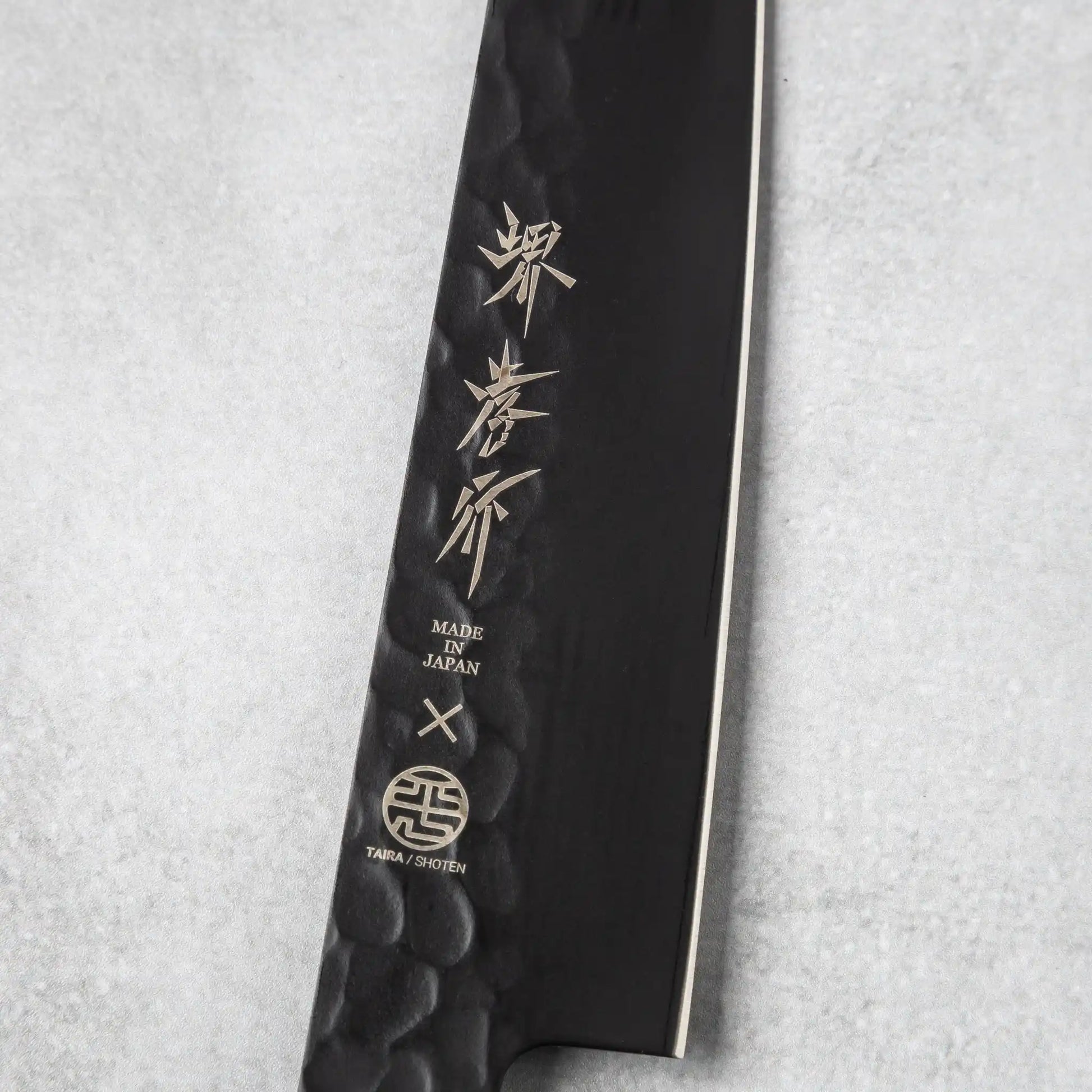 Close-up of the blade engraving on the Sakai Takayuki Kurokage VG10 petty knife, featuring Japanese characters and the "Made in Japan" emblem on the hammered black surface.